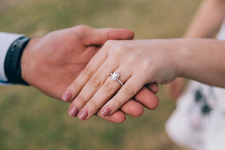 Couple holding hands with oval diamond engagement ring bordered by small diamonds